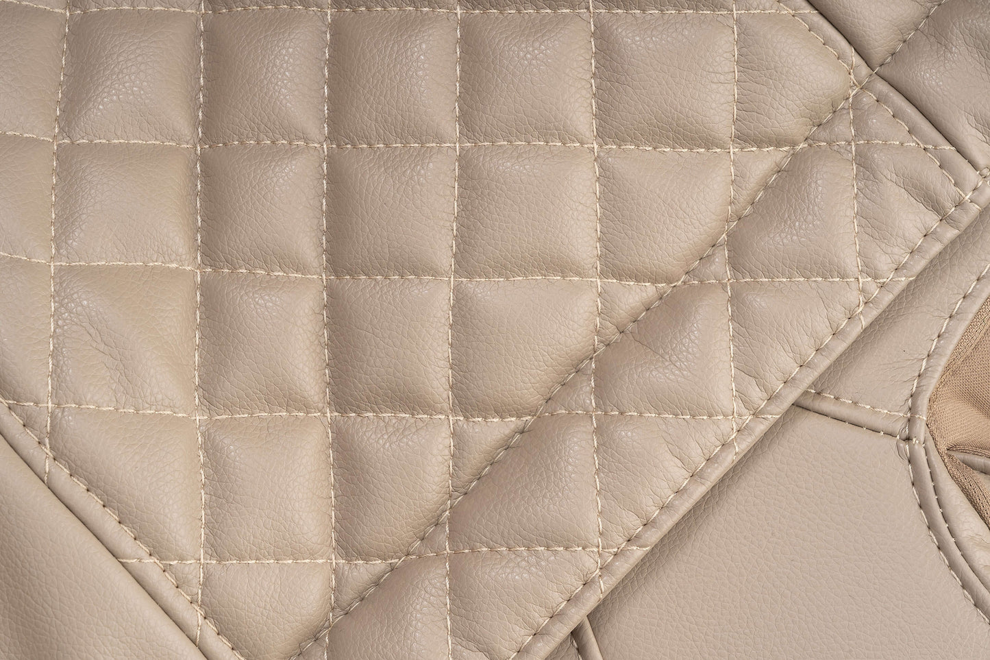 Close-up of beige quilted leather upholstery, showcasing luxurious texture and stitching detail.