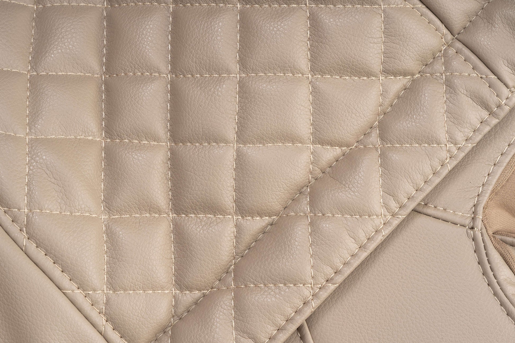 Close-up of beige quilted leather upholstery, showcasing luxurious texture and stitching detail.