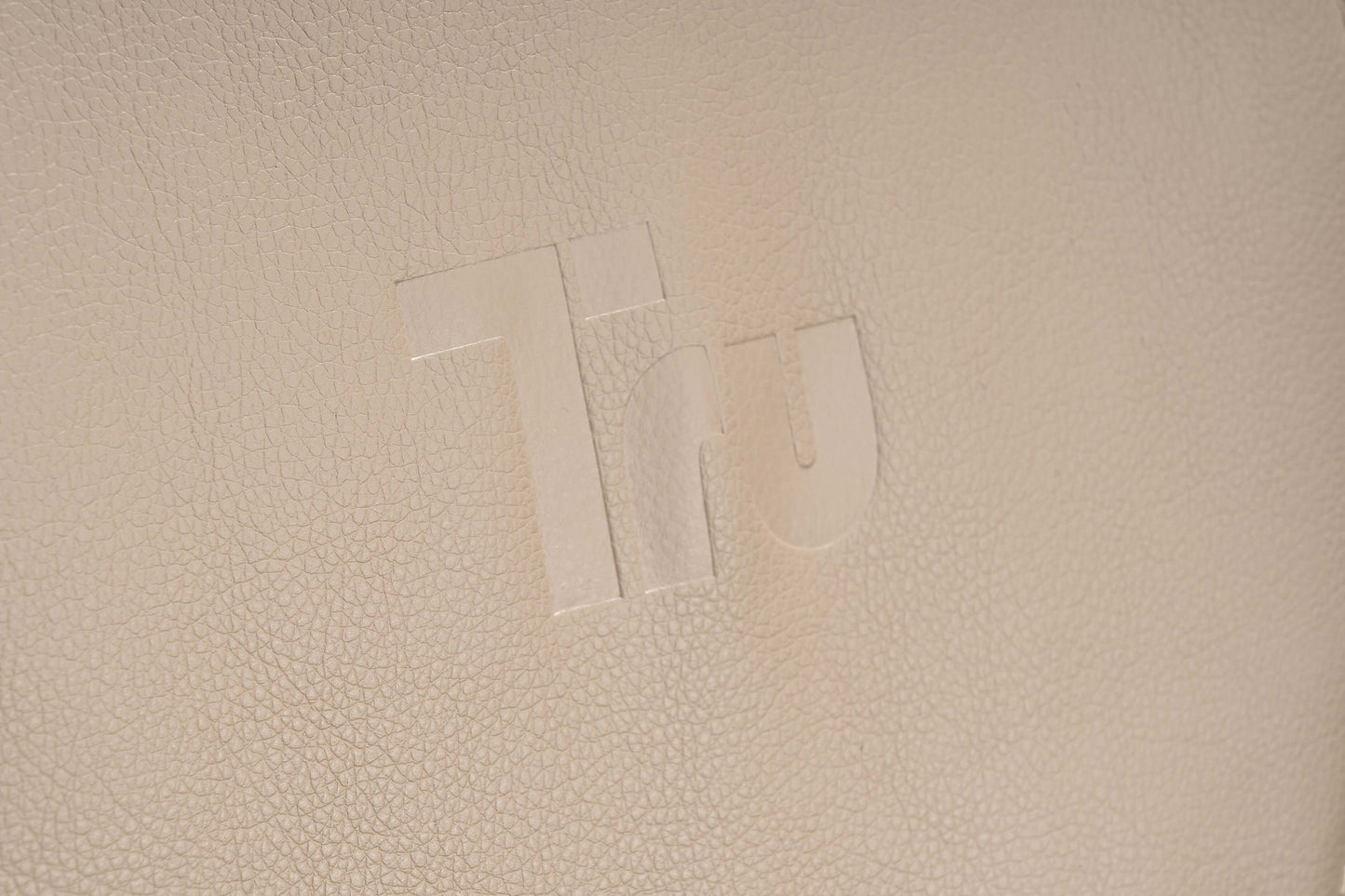 Close-up of the Tru logo embossed on cream leather fabric, signifying luxury and design quality.