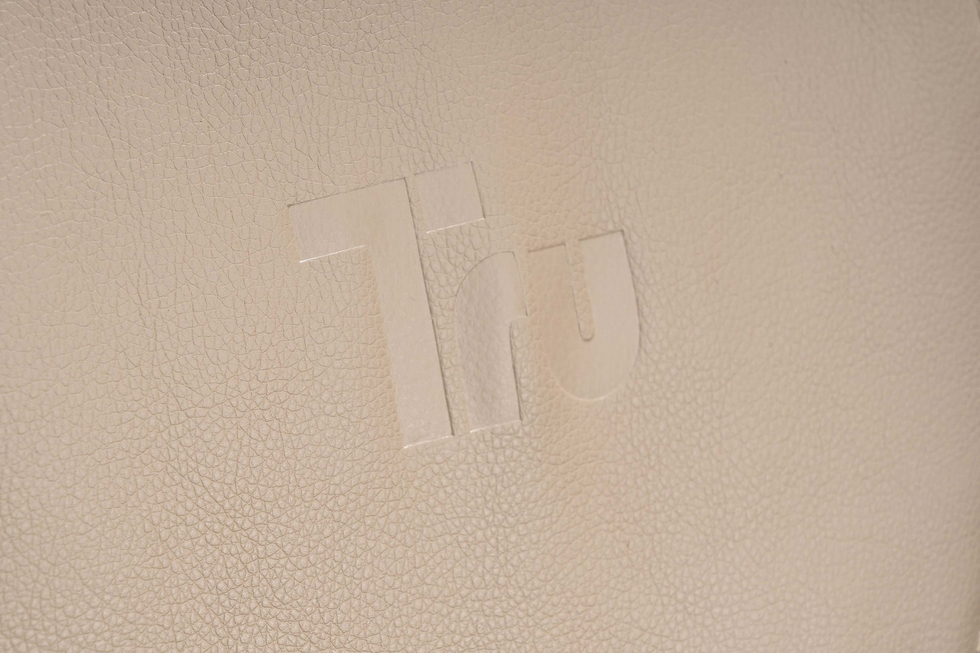 Close-up of the Tru logo embossed on cream leather fabric, signifying luxury and design quality.